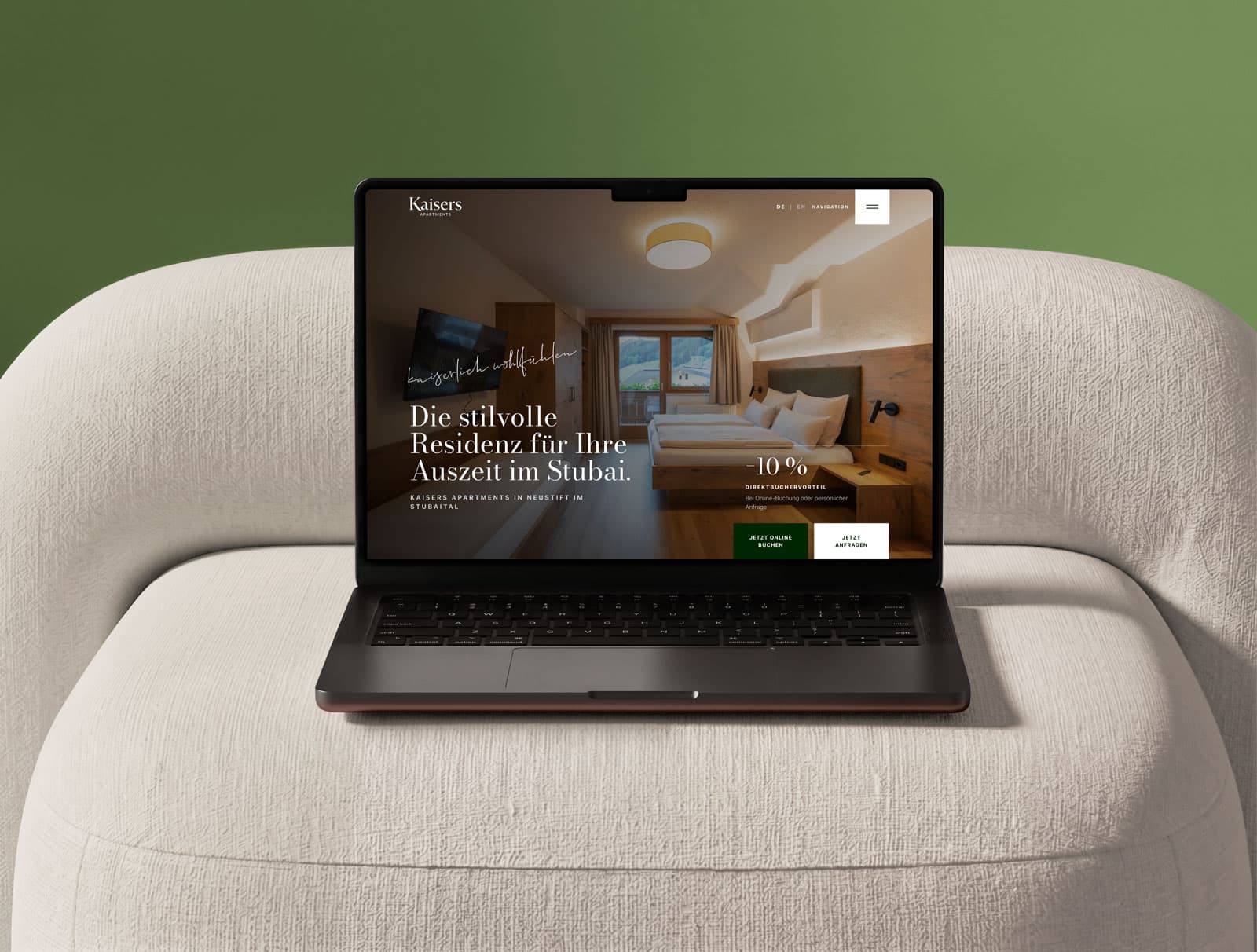 Laptop mit der Website von Kaisers Apartments auf einem hellen Sessel vor grünem Hintergrund